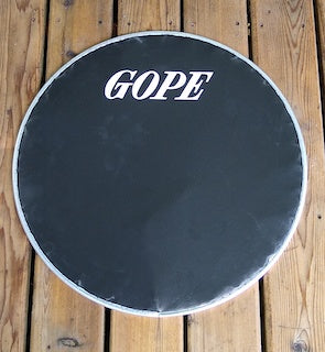 Black napa drum head on a wooden porch. Surdo head with aluminum rim and a GOPE logo