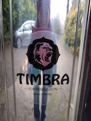 Timbra logo on the side of a polished aluminum surdo. You can see the photographer's reflection in the surdo shell.